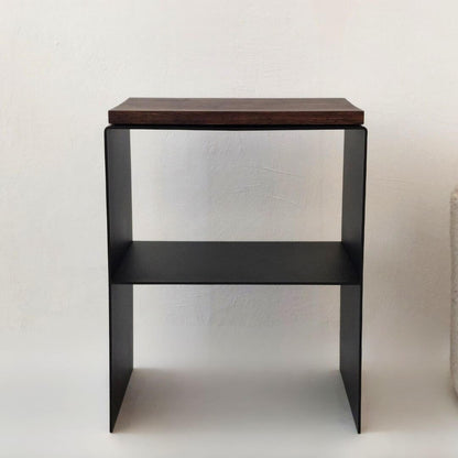 Juodas metalinis naktinis staliukas su mediniu viršumi šalia lovos